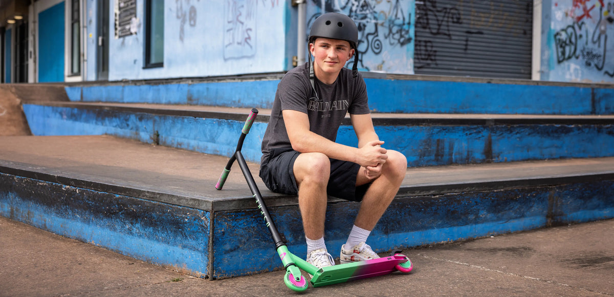 Child sitting on skateboards outdoors in autumn skatepark, representing half-term adventure activities for kids including scooters, skateboards and outdoor play in UK autumn weather.
