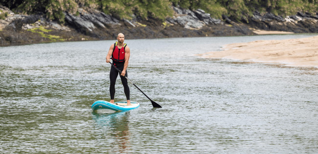 Man paddleboarding on calm water in South West England, exploring one of the top stand-up paddleboarding (SUP) adventure spots featured in the blog.