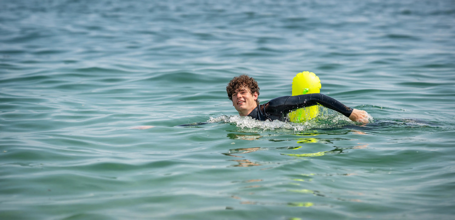 Beginner sea swimmer in wetsuit floating calmly in open water with bright safety float, demonstrating safe outdoor sea swimming techniques.