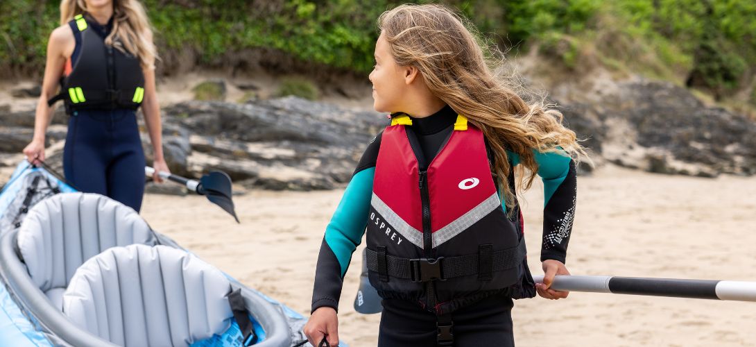 A photo of a girl in a red PFD carrying the front end of an inflatable kayak