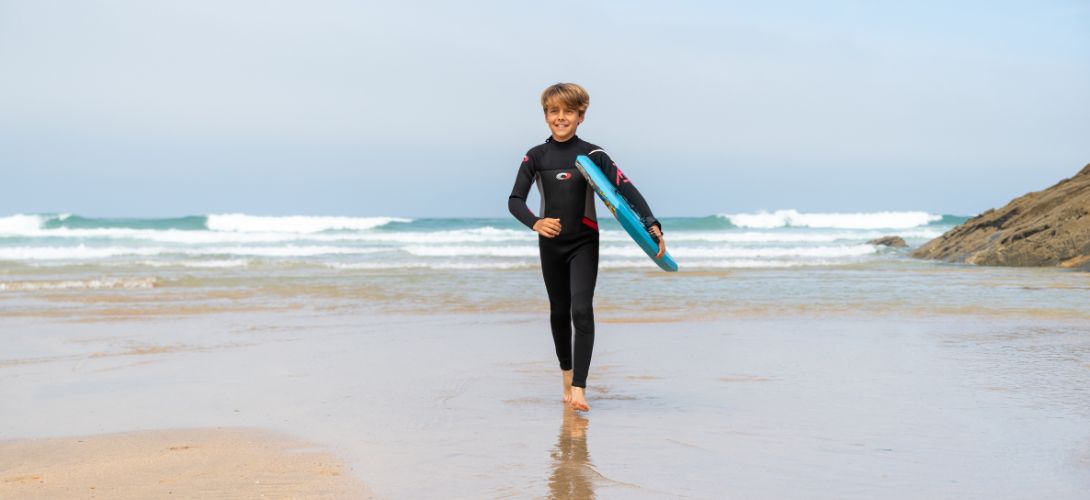 A photo of a boy running down the beach holding a blue bodyboard
