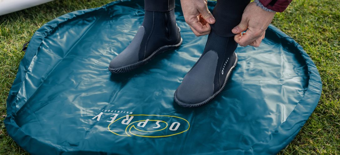 A close up image of someone adjusting wetsuit boots on a teal Osprey changing mat