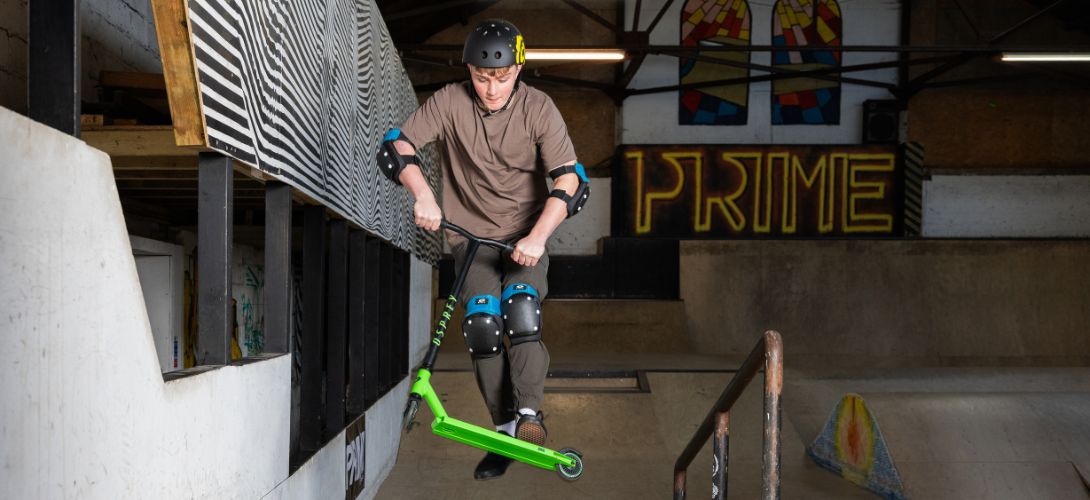 A photo of a boy performing a trick in the air on a blue stunt scooter