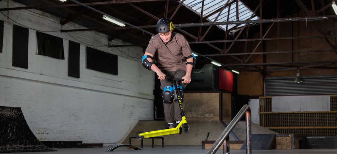 A man riding a yellow stunt scooter in an indoor skate park