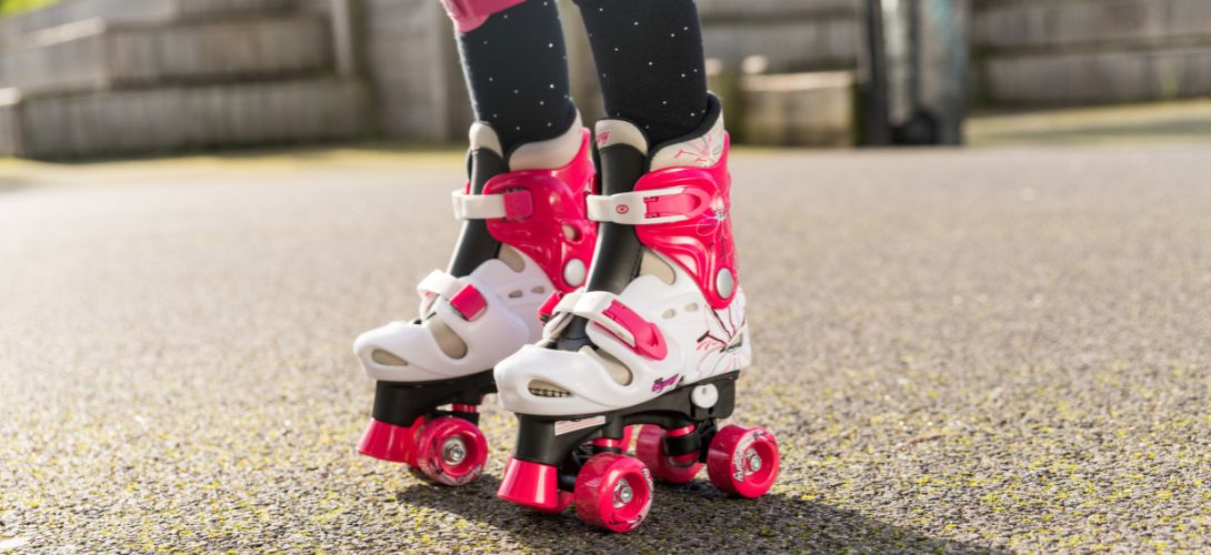 A close up image of a pair of kids pink and white quad roller skates