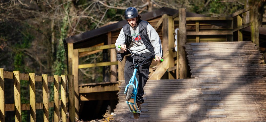 A man riding a blue dirt scooter along a wooden ramp