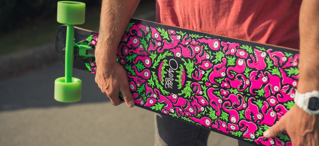 A close up image of a pink and green deck of a longboard