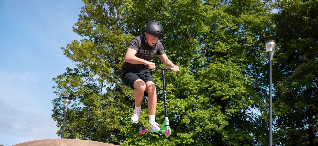 A young man performing a trick in the air on a pink and green stunt scooter