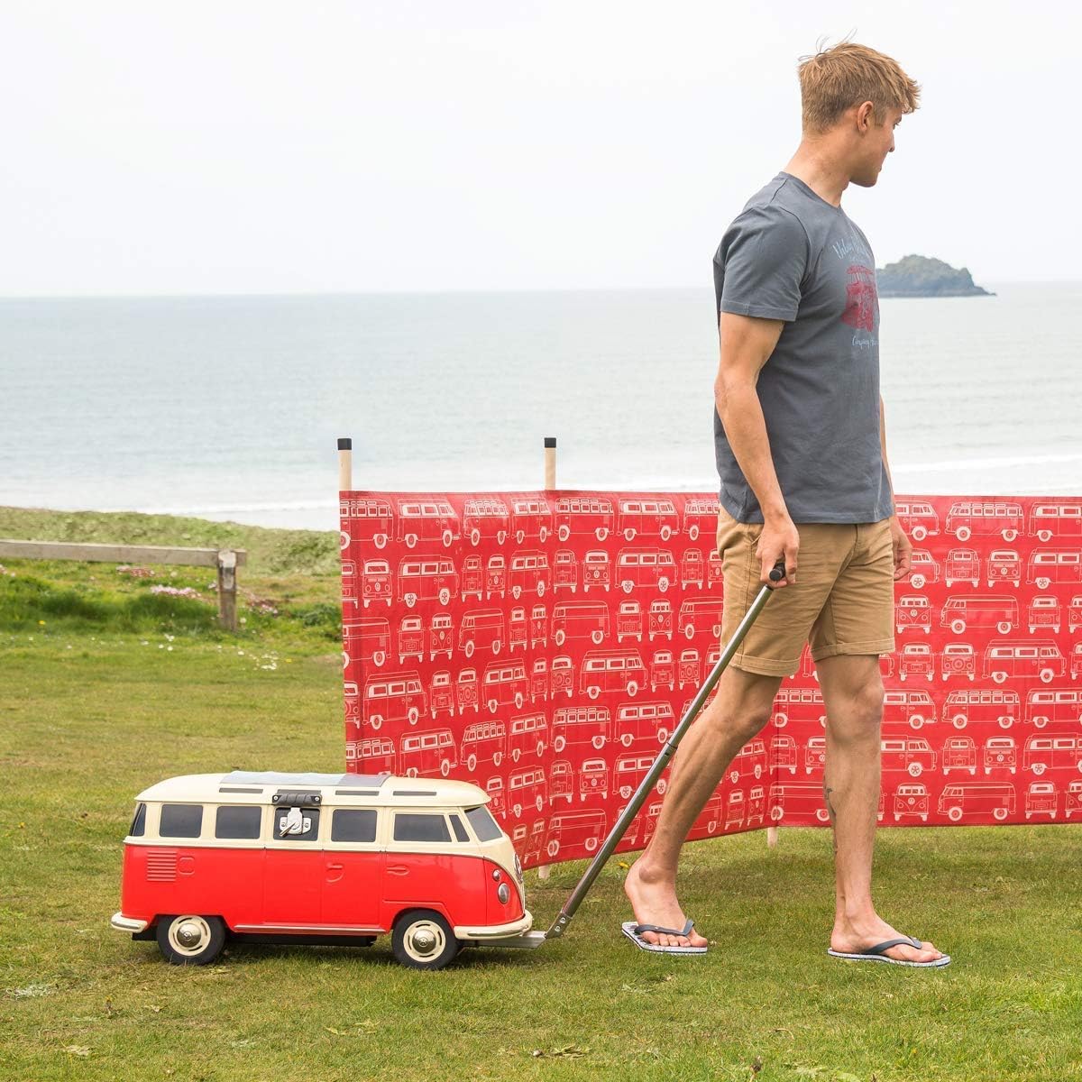Man standing next to a red and white volkswagen camper van with a scenic background