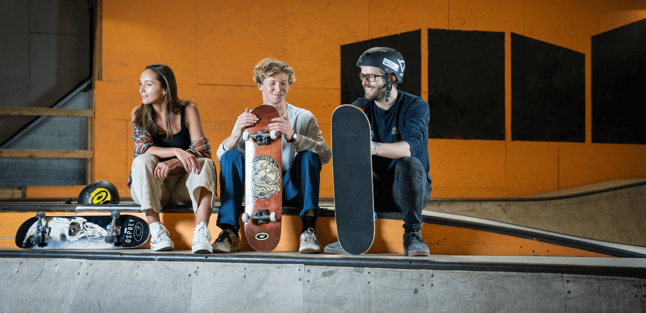 Three skateboarders sitting together at a UK skatepark with their Osprey skateboards, taking a break during a skate session – featured in a blog about the top skateparks in the UK.