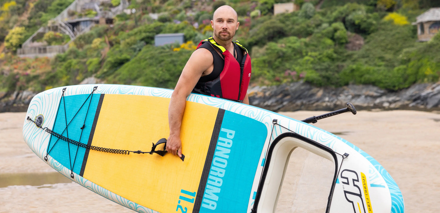 Paddleboarder holding a board at the coast, demonstrating progression from beginner to confident stand up paddleboarding in UK waters.