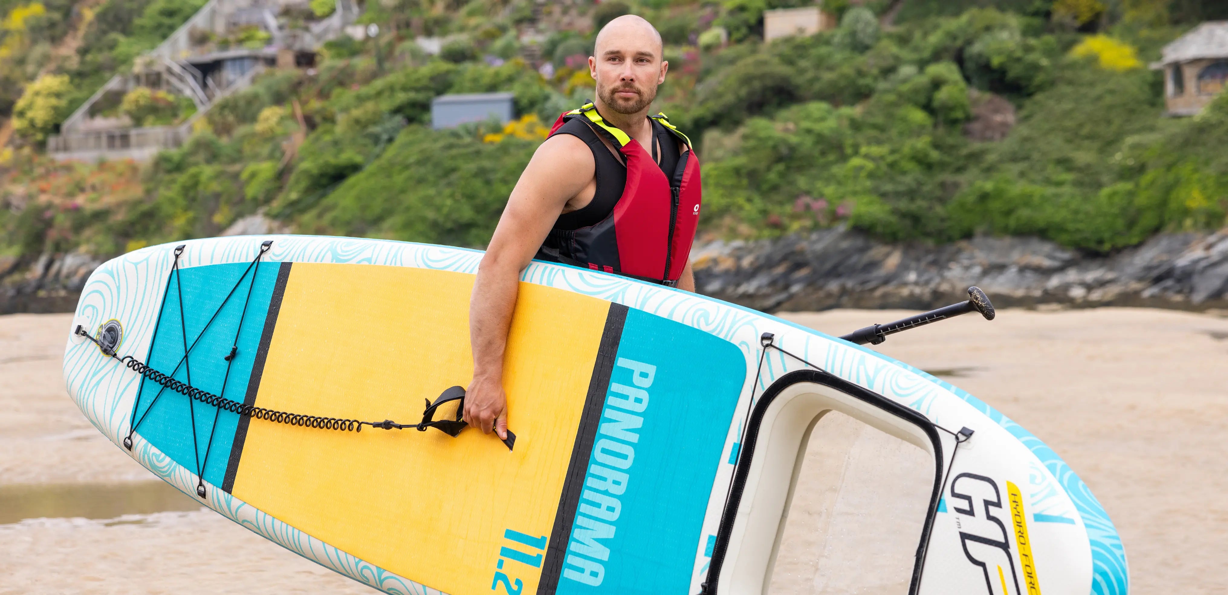 Paddleboarder holding a board at the coast, demonstrating progression from beginner to confident stand up paddleboarding in UK waters.