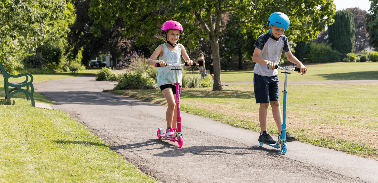 Children scooting through a park on Osprey scooters, part of a blog about the best adventure activities for half term.
