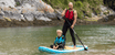 Man and child wearing PFDs while paddleboarding on calm water, demonstrating essential paddleboard safety practices.
