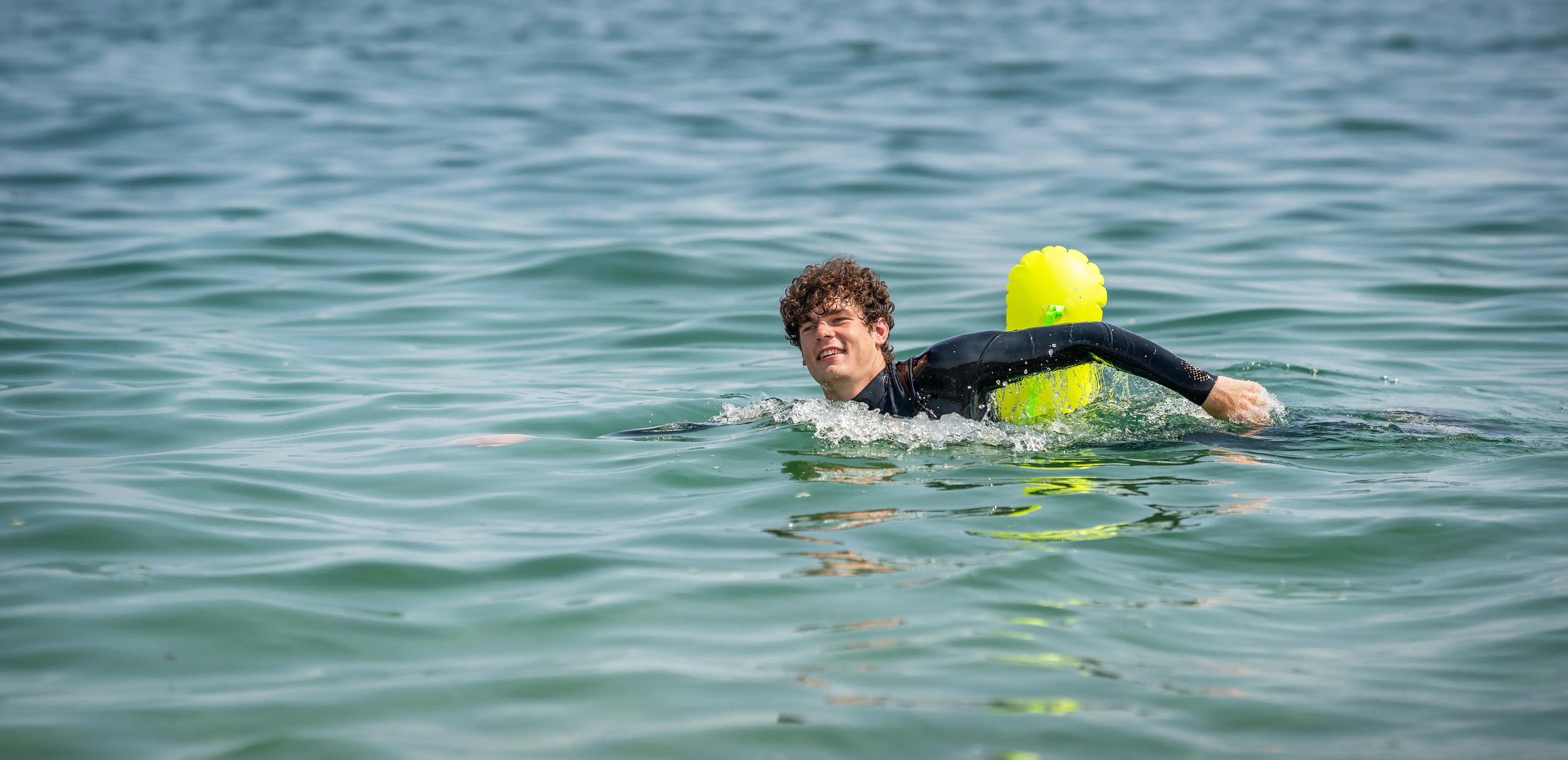 Beginner sea swimmer in wetsuit floating calmly in open water with bright safety float, demonstrating safe outdoor sea swimming techniques.