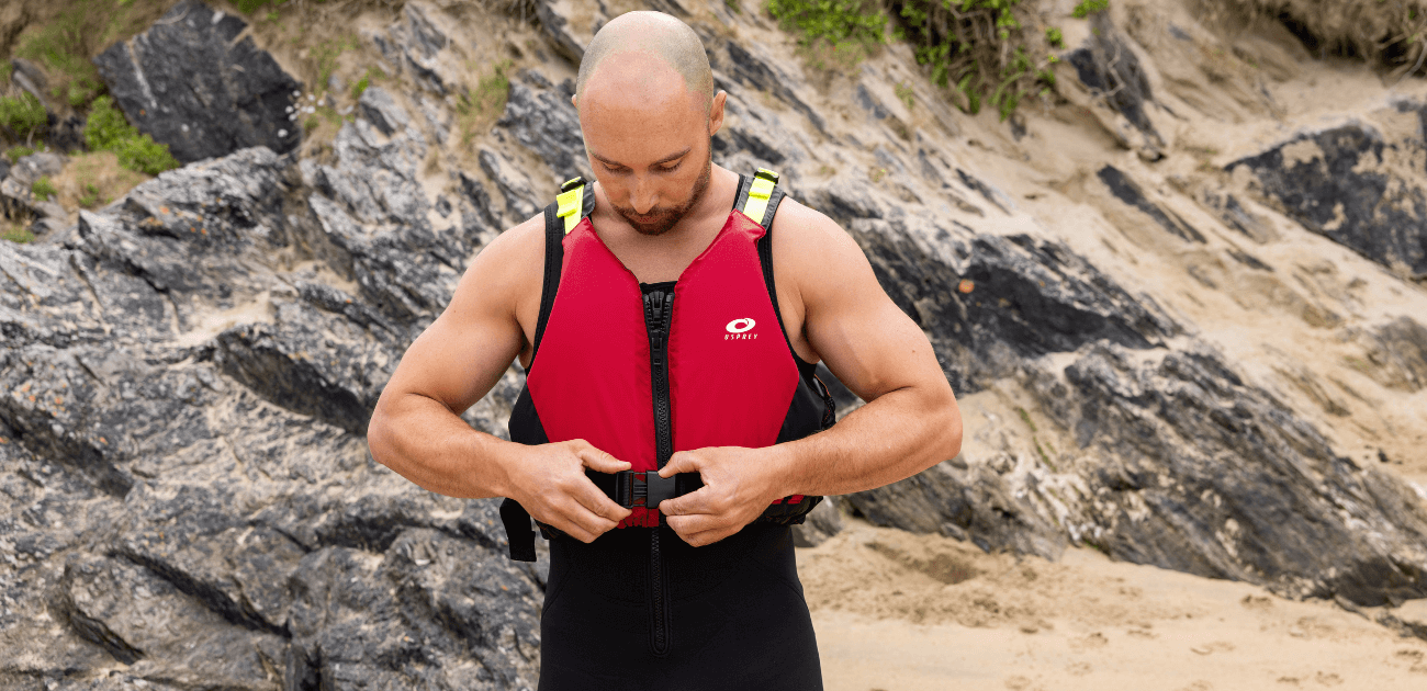 Man wearing an Osprey PFD on the beach, highlighting the benefits of wearing a buoyancy aid for safety during water sports.