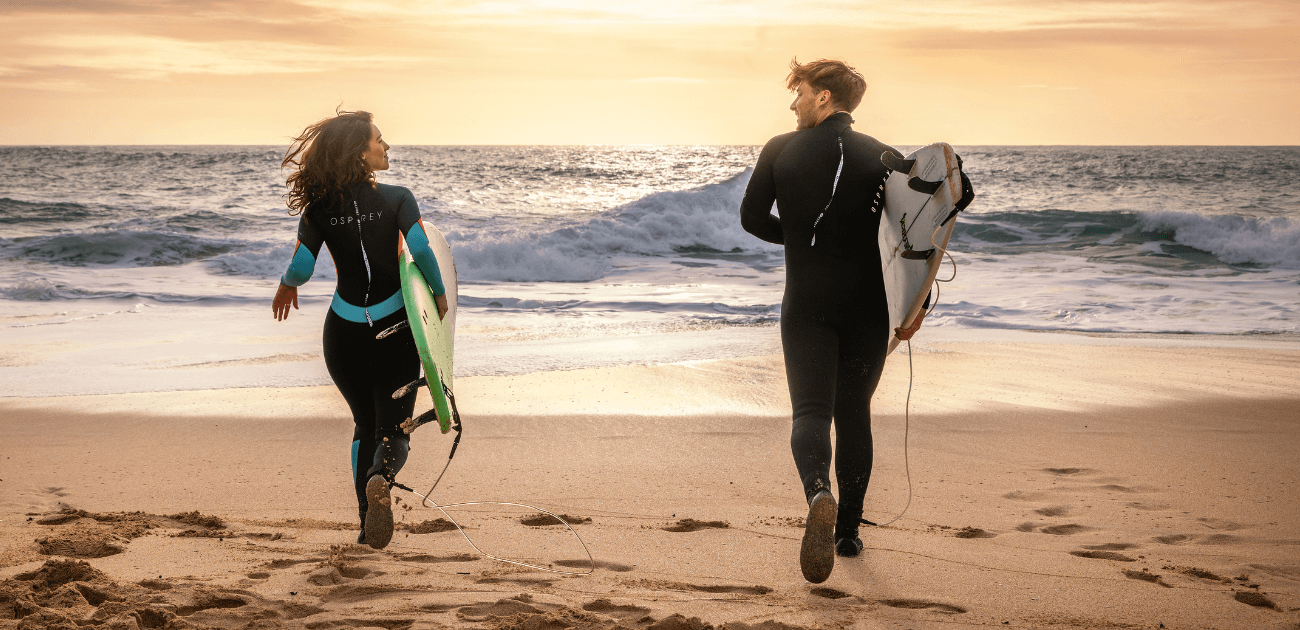 Two people running into the sea at sunrise wearing Osprey wetsuits, embracing ocean therapy for mental wellbeing
