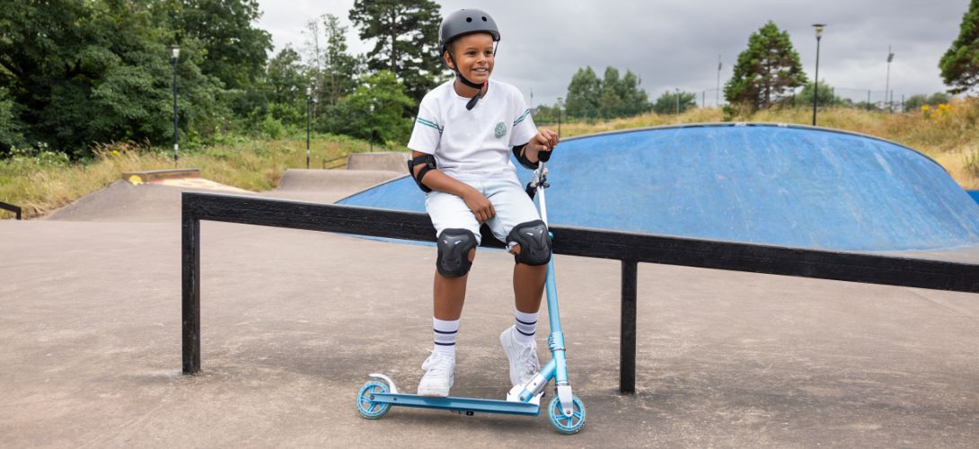 A photo of a boy sat at a skate park holding a blue Osprey buzz scooter