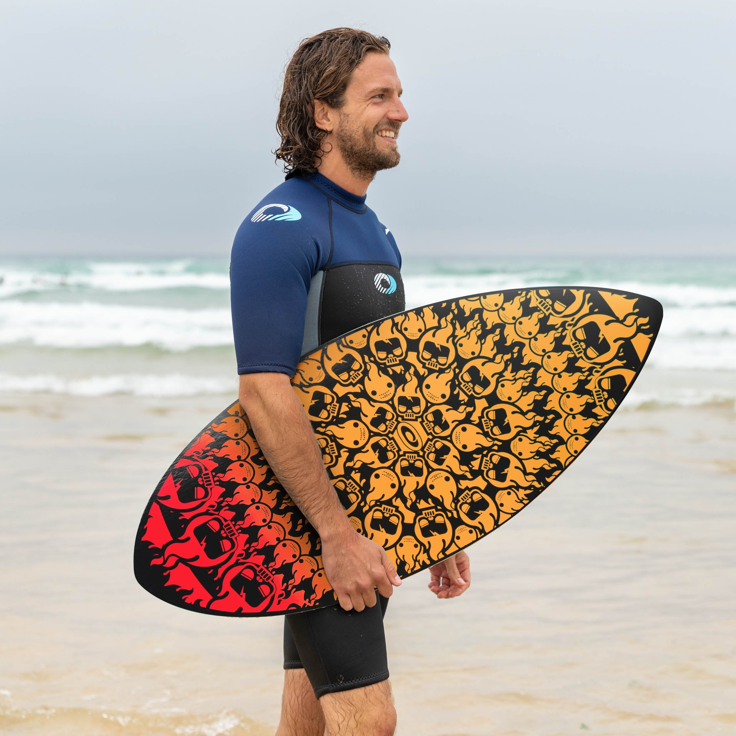 man in a shorty wetsuit holding his osprey skimboard on a uk beach