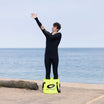 man in a wetsuit standing in a yellow, collapsible, changing bucket by the sea